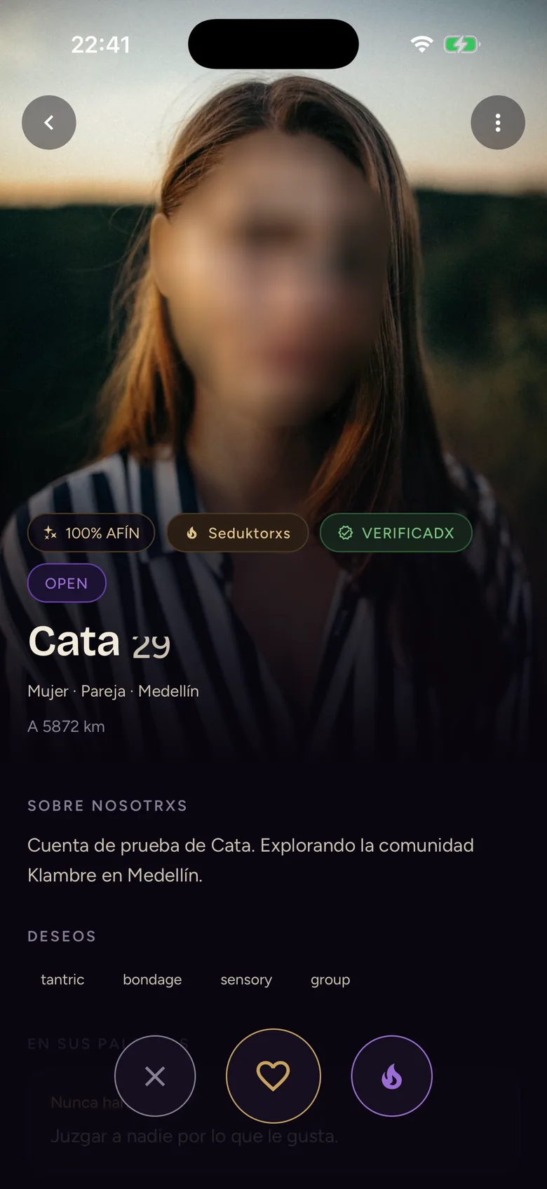 Ficha de perfil en Klambre: la foto con la cara difuminada, el porcentaje de afinidad, los sellos de vibe y de verificadx, la distancia aproximada y los botones de descartar y de dar me gusta.